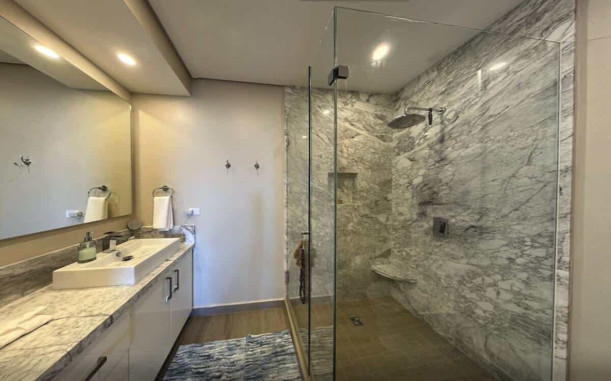 A modern bathroom with a glass-enclosed shower, marble walls, and a dual sink vanity.