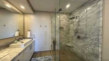A modern bathroom with a glass-enclosed shower, marble walls, and a dual sink vanity.
