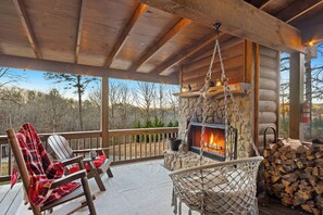 Une terrasse en bois avec une cheminée en pierre, un fauteuil suspendu et une pile de bois de chauffage.