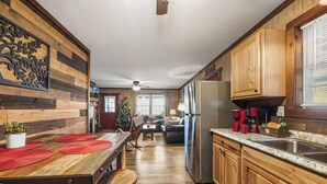 A kitchen with wooden cabinets, a stainless steel refrigerator, a wooden dining table with red placemats, and a Christmas tree in the background.