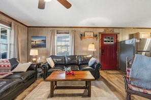 A cozy living room with a leather sofa, a wooden coffee table, and a red door.