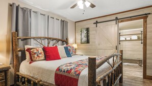A rustic wooden bed with a headboard, a ceiling fan, and a view of a wooden sliding door leading to a bathroom.