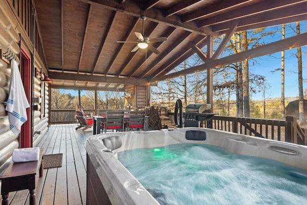A wooden deck with a hot tub, outdoor seating, and a grill.