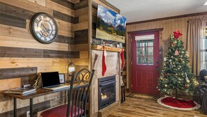 A cozy room with a wooden wall, a fireplace, a Christmas tree, and a red door.