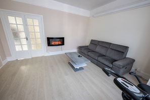 A living room with a grey sofa, a coffee table, a fireplace, and a stationary exercise bike. - La maison des Ducs, terrace, BBQ, Near the center (Nevers)