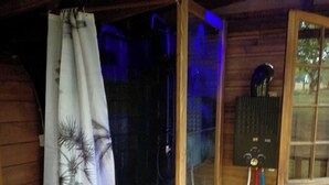 A wooden cabin with a shower area, a window, and a power outlet with cables.