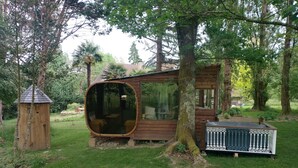 A wooden cabin with a large circular window, a small porch, and a fenced deck area.