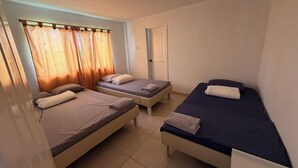 A small, clean room with three single beds arranged in a row, a door, and a window with curtains. - Beautiful countryside stay at La Milonga Finca Hotel with nature views (Montenegro)