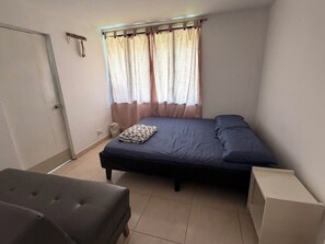 A small, neatly arranged bedroom with a single bed, a bedside table, and a chair.