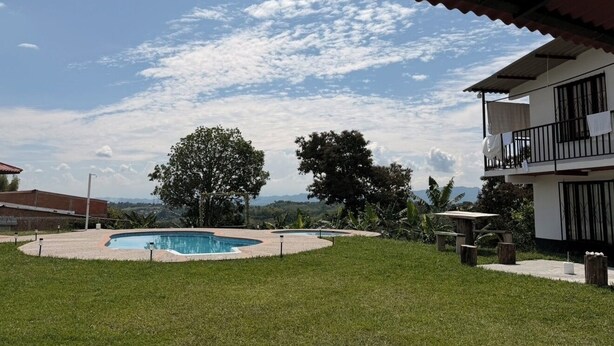 A swimming pool with a surrounding deck, a two-story building with balconies, and a view of distant hills. - Beautiful countryside stay at La Milonga Finca Hotel with nature views (Montenegro)