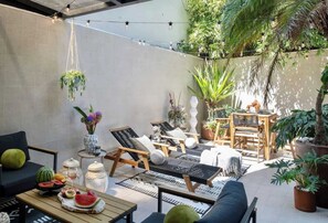 Eine sonnendurchflutete Terrasse mit Sitzgelegenheiten, Blumentöpfen und einer Lichterkette.