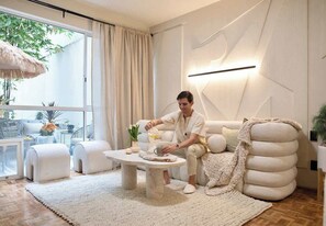 Ein modernes Wohnzimmer mit einer Couch, Hocker, einem Couchtisch und einem großen Fenster mit Vorhängen.