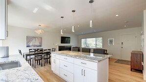 Een moderne keuken met een marmeren aanrechtblad, witte kasten en hanglampen.