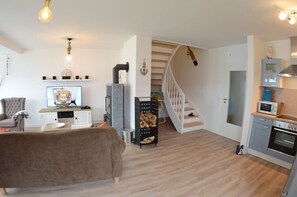 A modern living room with a sofa, TV, and fireplace. A staircase leads to a kitchen with appliances.