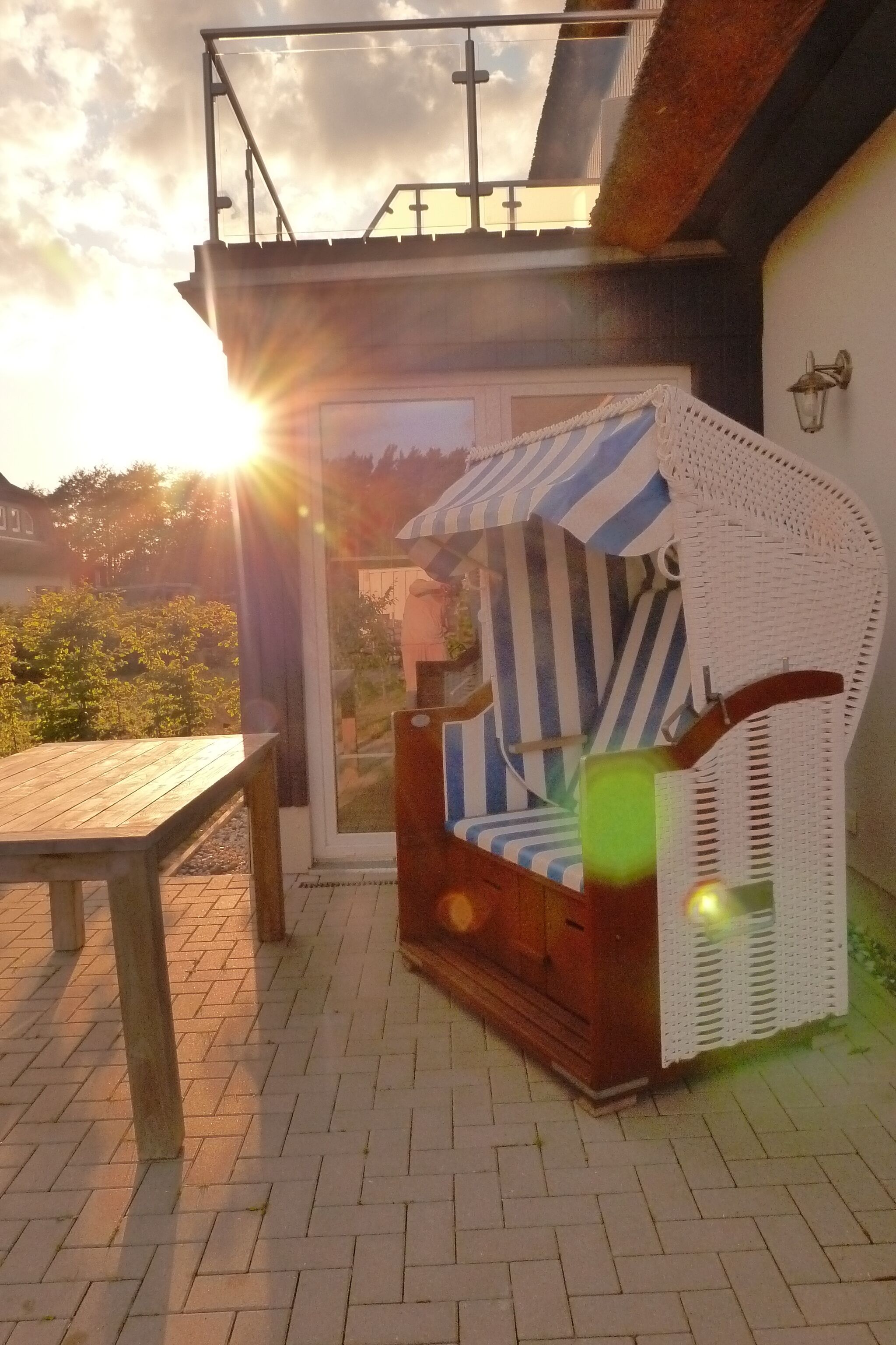 Ein Korbstuhl mit gestreifter Sitzkissen auf einer Terrasse.