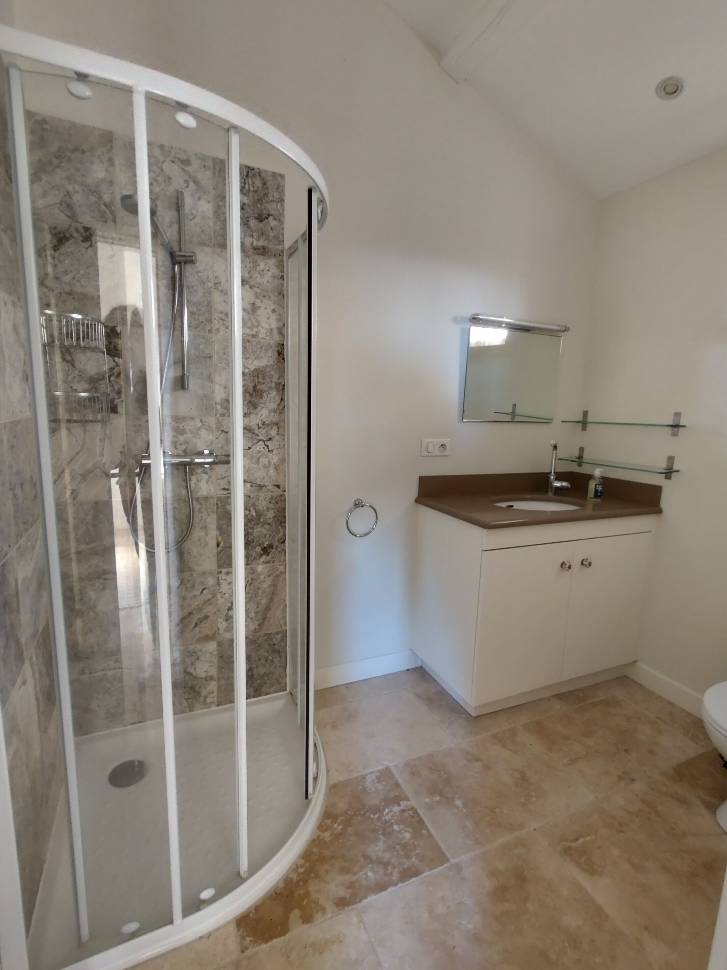 A bathroom with a glass-enclosed shower, a sink with a mirror above it, and tiled flooring.