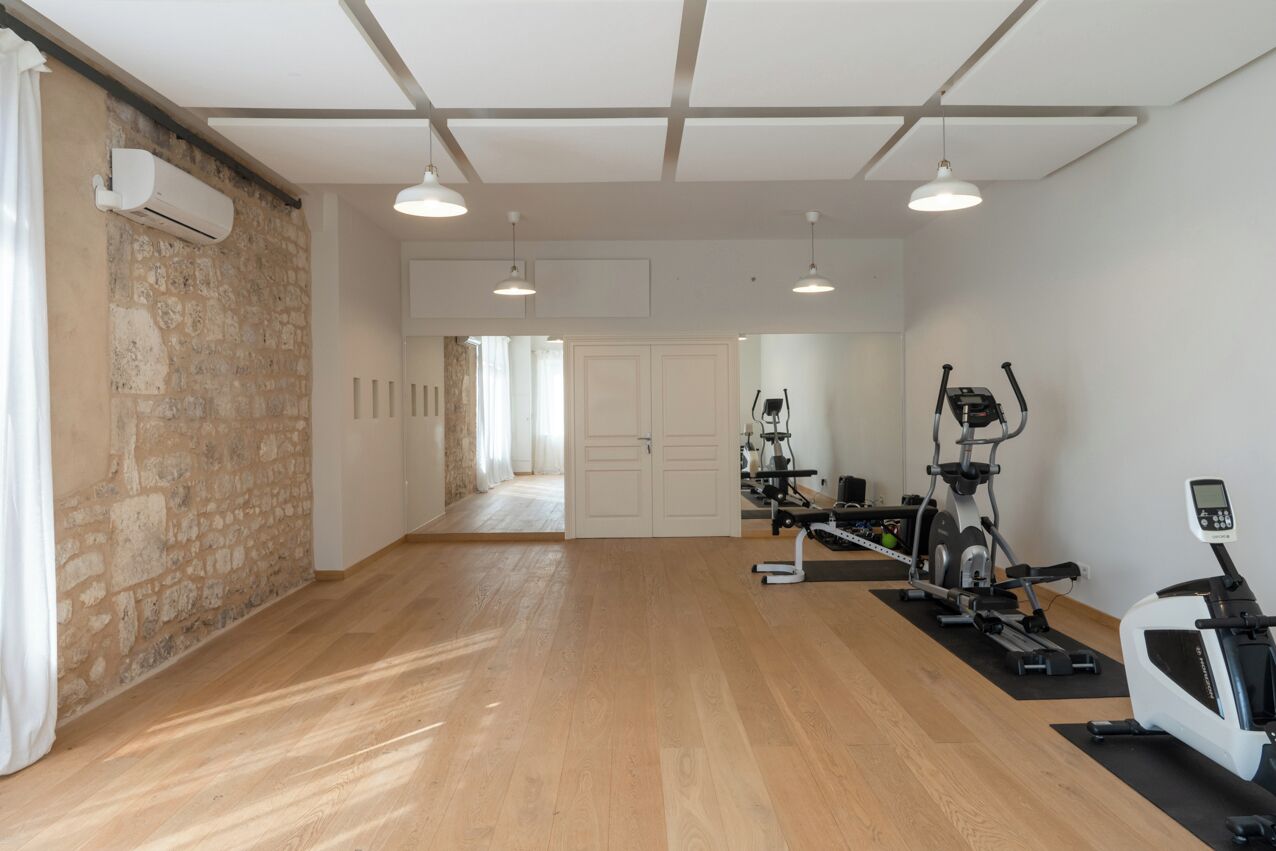 Ruime kamer met houten vloer, een stenen muur en een plafond met zichtbare balken. Er staan twee trainingsfietsen en een loopband.