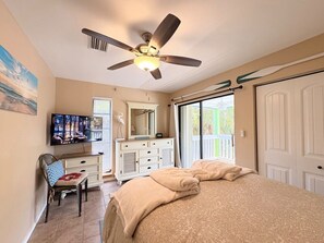 A bedroom with a bed, a desk with a television, a ceiling fan, and a sliding glass door to the outside. - Blue Macaw North Captiva Island (North Captiva)