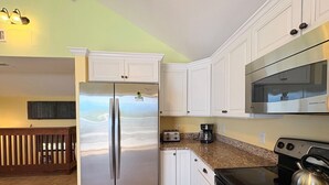 Una cocina con armarios blancos, un refrigerador de acero inoxidable, un microondas y una estufa.