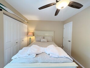 Ein Schlafzimmer mit einem Bett, einem Deckenventilator und einem Nachttisch mit Lampe.