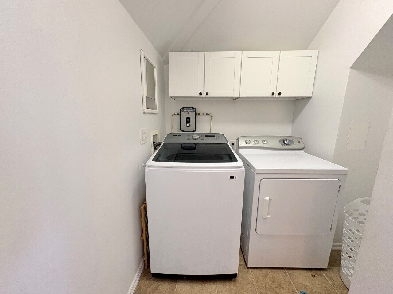 A laundry room with a front-loading washer and dryer, white cabinets above, and a small window.