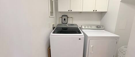 A laundry room with a front-loading washer and dryer, white cabinets above, and a small window.