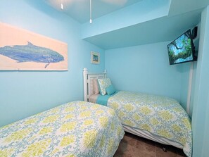 Ein Schlafzimmer mit zwei Betten, einem Fernseher an der Wand und einem Gemälde.