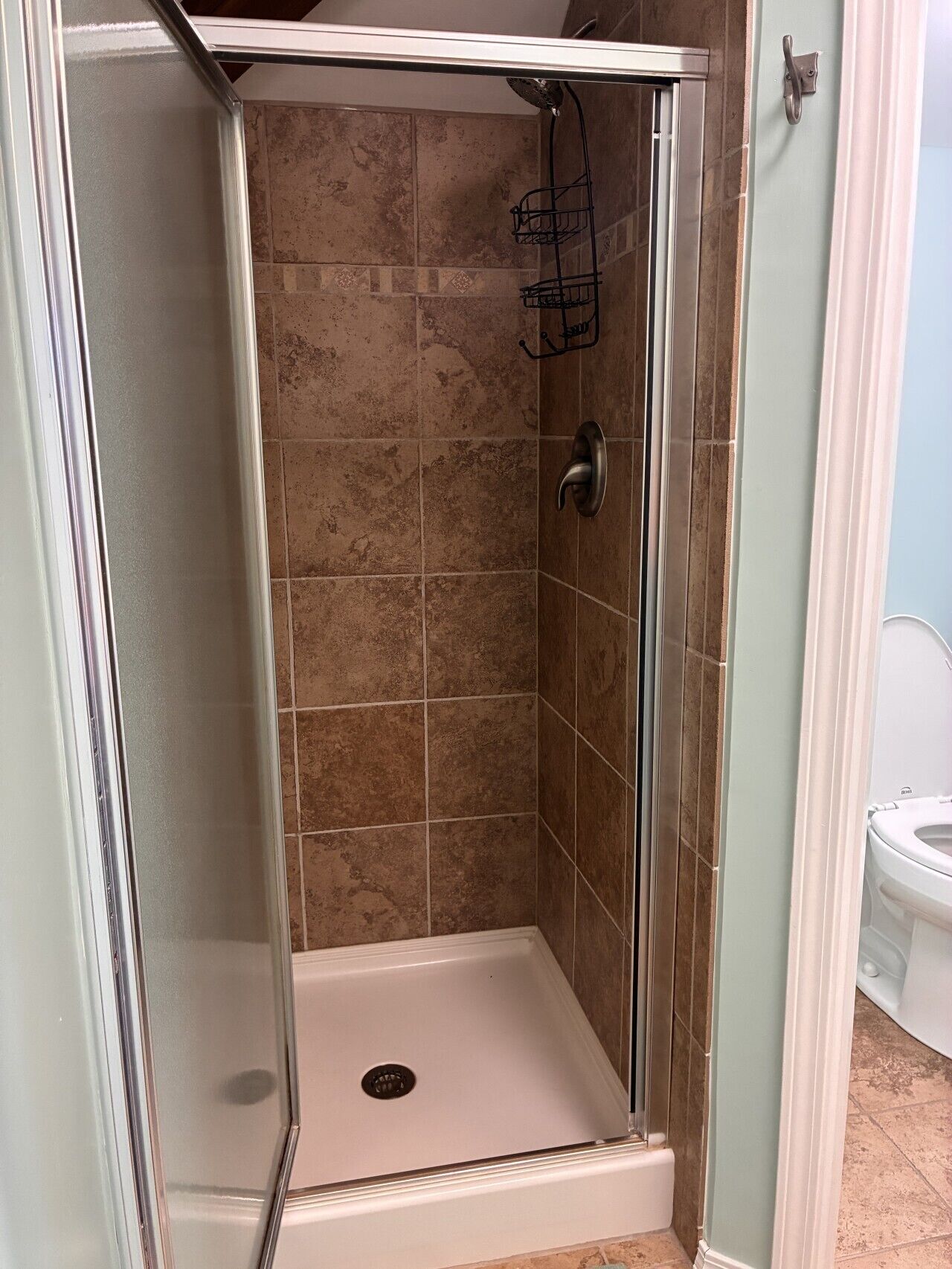 A shower with a glass door, a showerhead, and a handheld shower attachment.