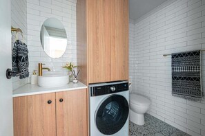 A modern bathroom with a white sink, wooden cabinets, a washing machine, and a toilet. - Magill Boho Retreat-2BR - free parking (Magill)