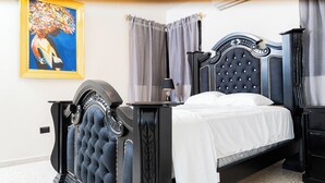A bedroom with a dark blue tufted headboard, a white bedspread, and a painting of a woman on the wall. - Private Luxury Escape  Villa Reina Bella Pool, Balcony & Sleeps 14 (Villa hermosa)