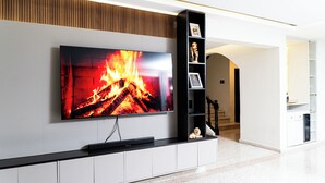 A modern living room with a large flat-screen TV mounted on a wall, a black entertainment unit below it, and a staircase leading to another level. - Private Luxury Escape  Villa Reina Bella Pool, Balcony & Sleeps 14 (Villa hermosa)