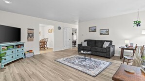 En moderne stue med et fladskærms-tv, en mørkegrå sofa, et mønstret tæppe og et træsofa-bord.