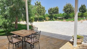 Eine Terrasse im Freien mit Tisch und Stühlen, umgeben von Grünpflanzen und blauem Himmel.