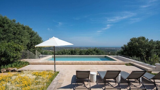 Ein Pool mit Blick, umgeben von Grün und einem weißen Sonnenschirm.