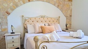 Ein Bett mit einem geblatteten Kopfteil, mehreren Kissen, einem Nachttisch mit einer Lampe und einer Steinwand.