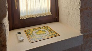 Ein Fenster mit dunklem Rahmen und weißem Vorhang, eine kleine Ablagefläche mit einer dekorativen Fliese und einer Fernbedienung darauf.