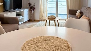 A modern living room with a round white table, a flat-screen TV, a sofa, and a view of the sea through large windows. - Alexis Beach (Pet Friendly) (Sarandë)