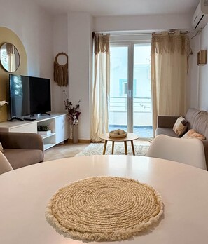 Ein modernes Wohnzimmer mit einem runden weißen Tisch, einem Flachbildfernseher, einer Couch und Meerblick durch große Fenster.