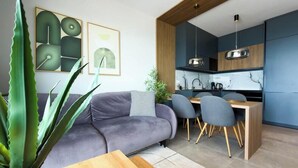 Un salon moderne comprenant un canapé, une table à manger, des chaises et un coin cuisine avec des placards et un luminaire suspendu.