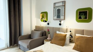Een hotelkamer met een bed, een slaapbank, een spiegel met groene lijst en een aan de muur hangend schilderij.