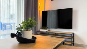 A modern room with a wooden table, a potted plant, a flat-screen TV mounted on the wall, and a sign indicating a WiFi code. - Amelia Beach (Pet Friendly) (Sarandë)