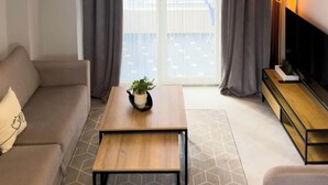 A modern living room with a sofa, a coffee table, a TV, and a large window with curtains. - Amelia Beach (Pet Friendly) (Sarandë)