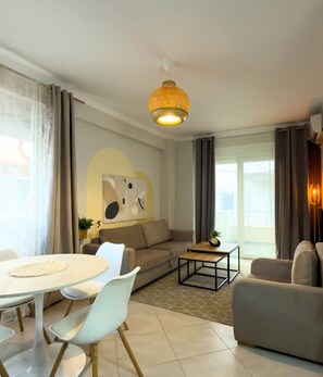 A modern living room with a sofa, a dining table with chairs, a coffee table, and a hanging light fixture. - Amelia Beach (Pet Friendly) (Sarandë)