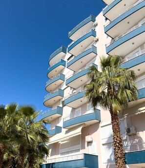 Un hôtel à plusieurs étages doté de balcons, de palmiers et surplombant un ciel d’un bleu limpide.