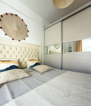 Ein Schlafzimmer mit einem gepolsterten Kopfteil, einem großen Spiegel und einem Bett mit vielen Kissen.