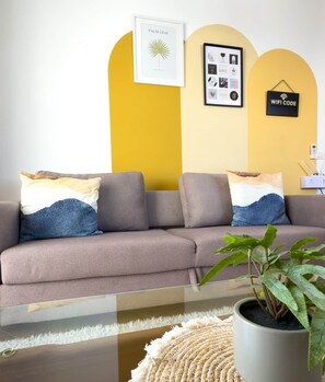 Ein modernes Wohnzimmer mit einem grauen Sofa, einem gerahmten Kunstwerk, einem WLAN-Symbol und einem Topfpflanzen.