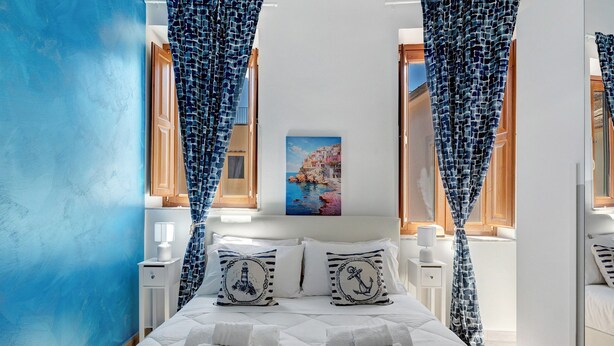 Ein Schlafzimmer mit Bett, Kissen, Nachttisch, Lampe und Vorhängen.