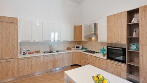 Eine moderne Küche mit weißen Schränken, einer zentralen Kochinsel und einem eingebauten Backofen.