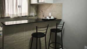 A modern kitchen with a black countertop, two black bar stools, a white sink, and a window with sheer curtains. - Aeroband (Núcleo Bandeirante)