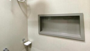 A shower with a handheld showerhead, a wall-mounted control panel, and a small shelf. - Aeroband (Núcleo Bandeirante)